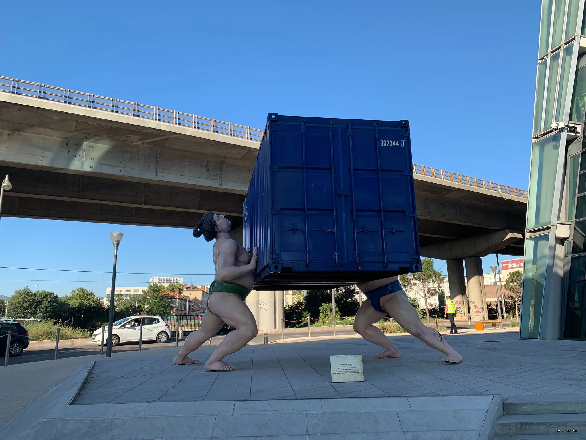Sculpture of sumo fighters lifting a container | Autor: Rberchie | Licencja: CC BY-SA 4.0 | Źródło: Wikimedia Commons