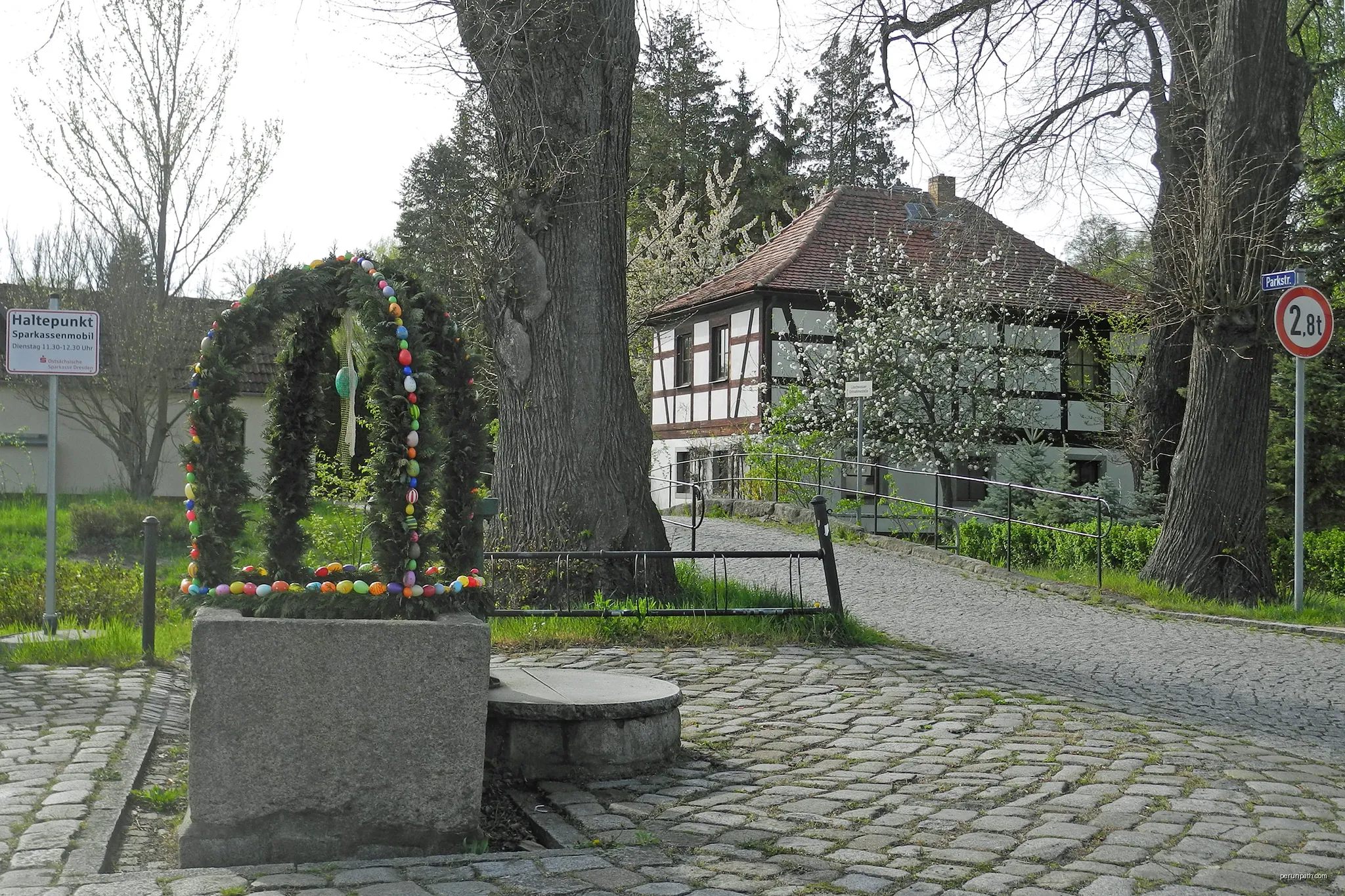 Osterbrunnen in Deutschbaselitz, Dorfplatz, mit Blick zum Gärtnerhaus | Autor: SchiDD | Licencja: CC BY-SA 4.0 | Źródło: Wikimedia Commons
