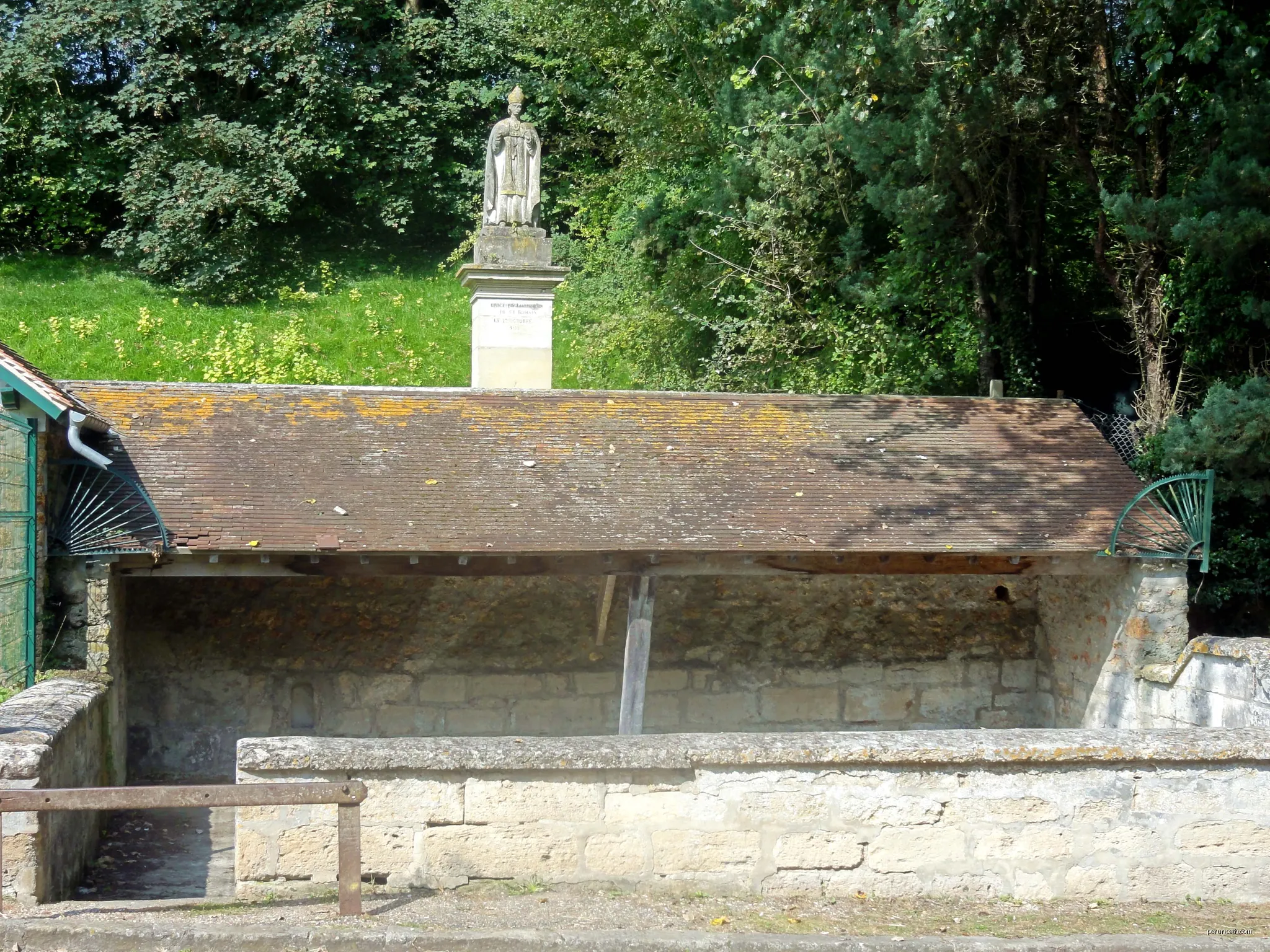 La fontaine Saint-Romain, aménagée en lavoir, accompagnée d'un abreuvoir et surplombée par une statue de Saint-Romain. Près de la RD 159 entre Guiry et Wy. | Autor: P.poschadel | Licencja: CC BY-SA 3.0 | Źródło: Wikimedia Commons